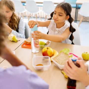 Kids having lunch together at school with sandwiches and fruits in a bright canteen.